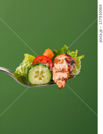 Perfectly composed close-up of a metal fork holding a healthy bite-sized sample of grilled chicken, sliced cucumber, cherry tomato, and fresh lettuce leaves. 137930069