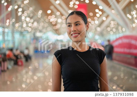A portrait of a smiling young Asian woman wearing a black t-shirt in a modern airport terminal 137931098