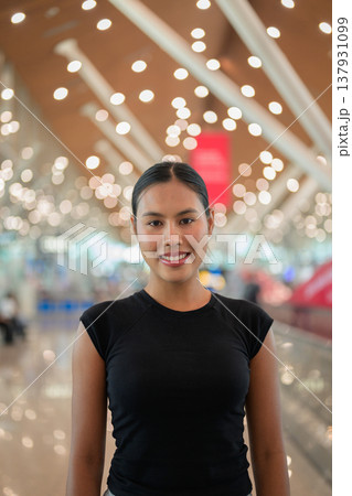 A portrait of a smiling young Asian woman wearing a black t-shirt in a modern airport terminal 137931099