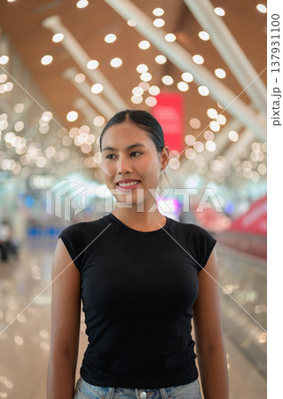 A portrait of a smiling young Asian woman wearing a black t-shirt in a modern airport terminal 137931100