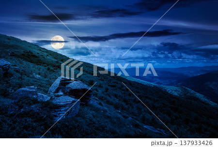 beautiful summer landscape in mountains at night. full moon over grassy hill with huge stones under the dark sky. mysterious nature background. picture of hillside meadow near the mountain peak 137933426