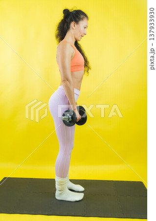 Woman exercising with dumbbells on mat building strength 137933930