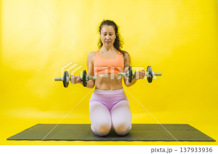 Woman exercising biceps with dumbbells on mat Woman exercising biceps with dumbbells on mat 137933936