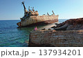 Tourist sitting on a rocky cliff watching the grounded rusty cargo ship EDRO III against the clear blue sky and turquoise Mediterranean Sea near Paphos, Cyprus 137934201