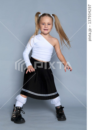 little girl strikes a playful pose with her fists raised near her chin during a studio shoot. Her fun, carefree expression and trendy outfit capture the essence of childhood joy and energy. 137934297