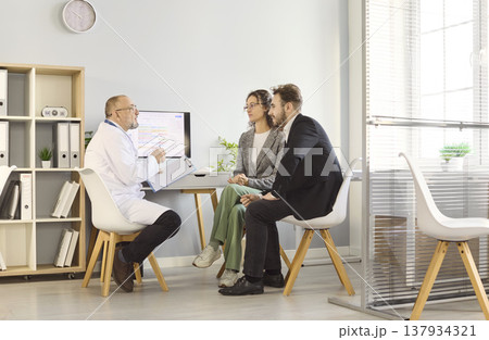 Doctor consulting couple in modern clinic, seated meeting about test results 137934321