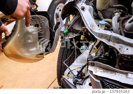 Car repair begins as person removes damaged car part from front of vehicle in garage Car repair begins as person removes damaged car part from front of vehicle in garage 137935263