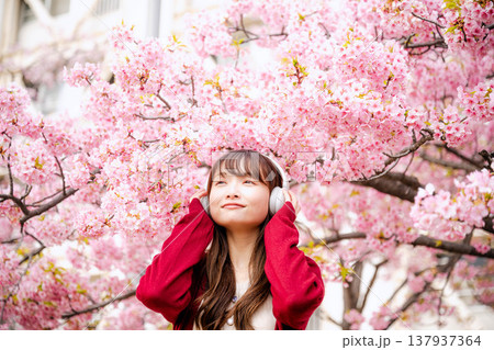 桜の中でヘッドホンで音楽を聴く若い女性 137937364