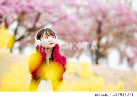 桜の中でヘッドホンで音楽を聴く若い女性 137937371