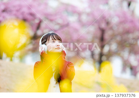 桜の中でヘッドホンで音楽を聴く若い女性 137937376
