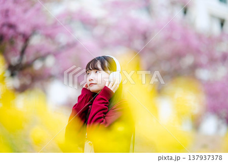 桜の中でヘッドホンで音楽を聴く若い女性 137937378