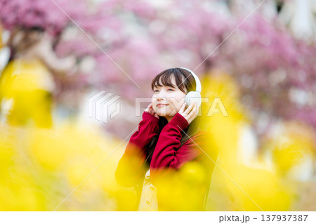 桜の中でヘッドホンで音楽を聴く若い女性 137937387