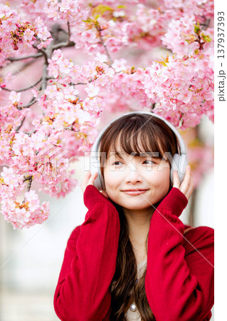 桜の中でヘッドホンで音楽を聴く若い女性 137937393