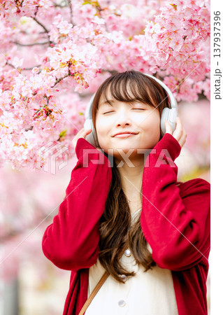 桜の中でヘッドホンで音楽を聴く若い女性 137937396