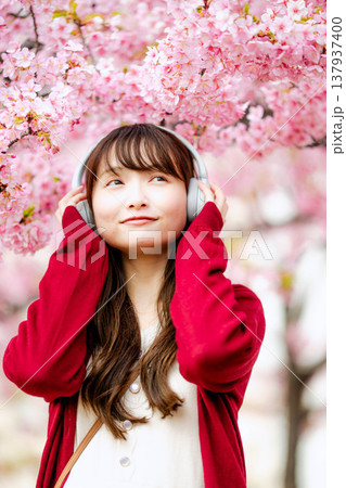 桜の中でヘッドホンで音楽を聴く若い女性 137937400