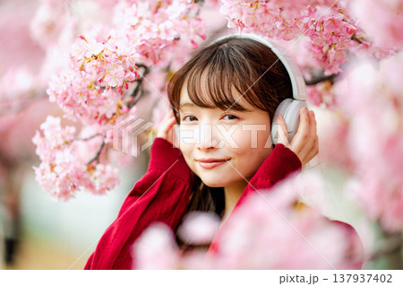 桜の中でヘッドホンで音楽を聴く若い女性 137937402