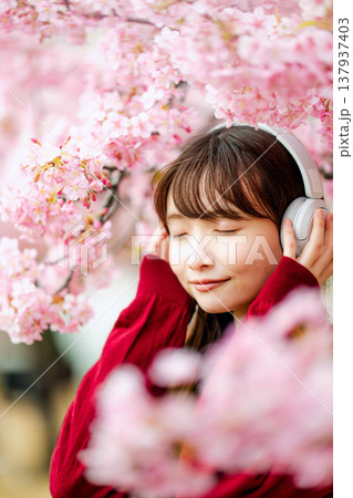 桜の中でヘッドホンで音楽を聴く若い女性 137937403