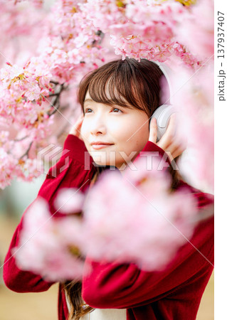 桜の中でヘッドホンで音楽を聴く若い女性 137937407