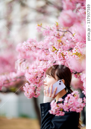 桜の前でスマートフォンで通話する若い女性 桜の前でスマートフォンで通話する若い女性 137937589
