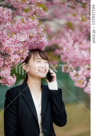 桜の前でスマートフォンで通話する若い女性 桜の前でスマートフォンで通話する若い女性 137937594