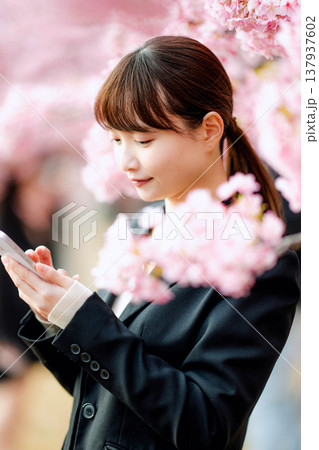 桜の前でスマートフォンで通話する若い女性 137937602