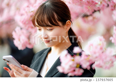桜の前でスマートフォンで通話する若い女性 桜の前でスマートフォンで通話する若い女性 137937605