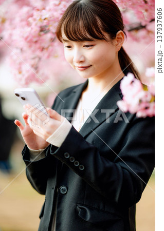桜の前でスマートフォンで通話する若い女性 桜の前でスマートフォンで通話する若い女性 137937606