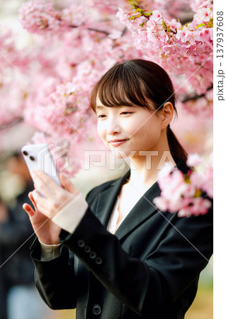 桜の前でスマートフォンで通話する若い女性 桜の前でスマートフォンで通話する若い女性 137937608