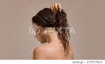 Woman holding wet curly hair in ponytail after washing 137937623