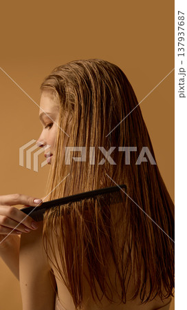 Woman combing wet hair with black comb on warm background. Woman combing wet hair with black comb on warm background. 137937687