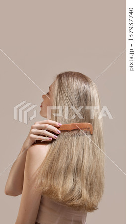 Woman brushing long smooth blonde hair with wooden comb on neutral background. Woman brushing long smooth blonde hair with wooden comb on neutral background. 137937740