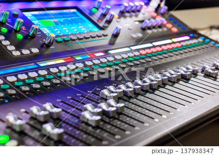 Sound mixing console is being used in studio setting at lights controls are active. Sound mixing console is being used in studio setting at lights controls are active. 137938347