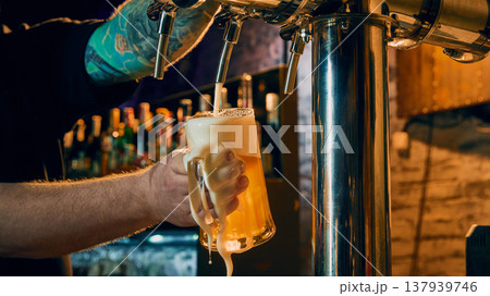 Bartender pouring draft beer into glass mug with foam dripping in bar close up Bartender pouring draft beer into glass mug with foam dripping in bar close up 137939746