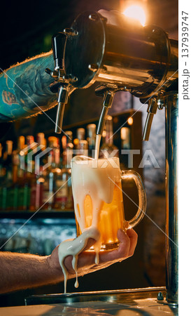 Draft beer pouring into glass mug with excessive foam spilling over bartender hand Draft beer pouring into glass mug with excessive foam spilling over bartender hand 137939747