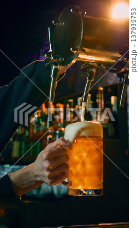 Bartender pouring cold draft beer into large mug with thick foam close up. Bartender pouring cold draft beer into large mug with thick foam close up. 137939753