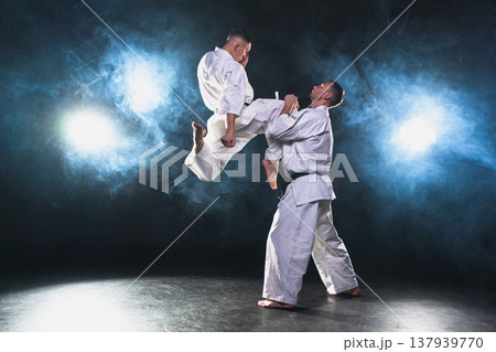 Martial arts masters on dark background. Strong man fighters in white kimono for karate martial arts fighting training in black gym. Karate fighters training punches kicks practicing fight sparring 137939770
