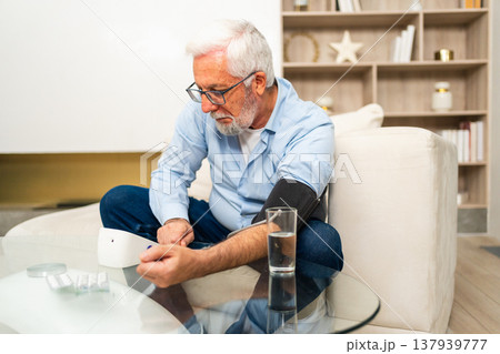 Hypertension problem in senior age. Old man measuring blood pressure with tonometer at home. Senior man have health problem making self checkup. Headache treatment of hypertension hypotension 137939777