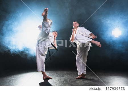 Martial arts masters on dark background. Strong man fighters in white kimono for karate martial arts fighting training in black gym. Karate fighters training punches kicks practicing fight sparring 137939778