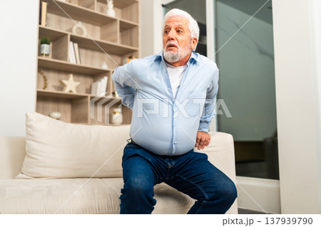 Backache back pain. Unhappy senior old man suffering from backache at home. Upset elder man feel sudden back pain muscles ache tension injury. Sad grandfather feeling pain hurt in back touching spine 137939790