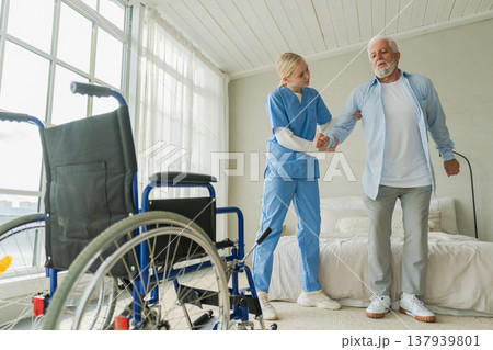 Rehabilitation healthcare. Physiotherapist nurse helps old man patient in wheelchair stand up walking. Man in chair for people with disability doing few steps with nurse helping. Medical caregiver 137939801