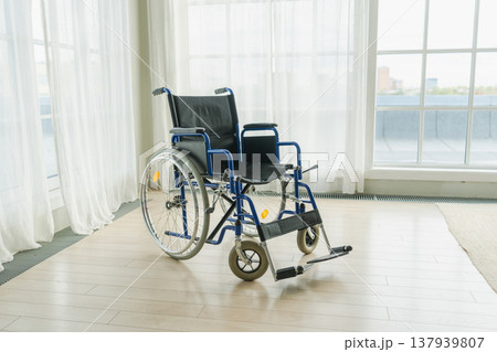 Empty wheelchair waiting for patient services in living room retirement home hospital. Chair for people with disability at home. Handicap accessible symbol. Health care medical lonely elderly sick Empty wheelchair waiting for patient services in living room retirement home hospital. Chair for people with disability at home. Handicap accessible symbol. Health care medical lonely elderly sick 137939807