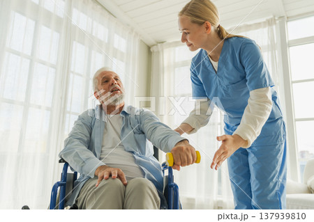 Support rehabilitation healthcare. Nurse helps old man patient in wheelchair picking up dumbbells. Paralyzed man in chair for people with disability doing sports exercise with nurse. Medical caregiver 137939810