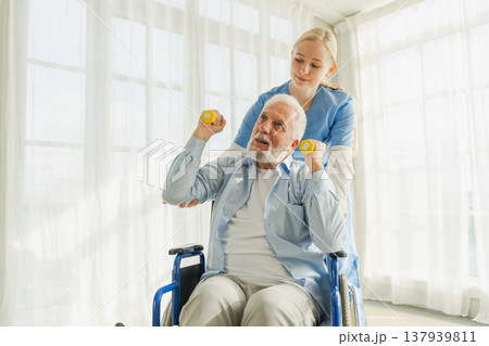 Support rehabilitation healthcare. Nurse helps old man patient in wheelchair picking up dumbbells. Paralyzed man in chair for people with disability doing sports exercise with nurse. Medical caregiver 137939811