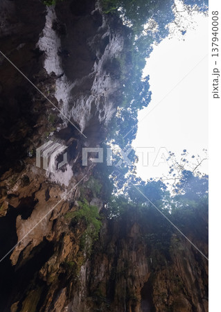 Upward view from inside Batu Caves near Kuala Lumpur, Malaysia. Showing a natural opening in the limestone cave with sunlight and greenery. 137940008