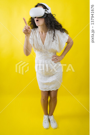 Woman experiencing virtual reality pointing finger with surprise Woman experiencing virtual reality pointing finger with surprise 137941676