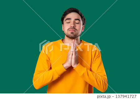 Young Man Praying With Fingers On Green Background. Guy Begs Satisfy Desires Young Man Praying With Fingers On Green Background. Guy Begs Satisfy Desires 137941727