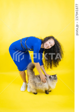 Happy woman petting fluffy cat on yellow studio background 137941877