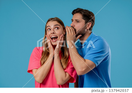 Gossiper man whispers in womans ear secret, rumors, gossips, blue studio. Pretty lady and handsome guy - couple, shh, conspiracy concept 137942037