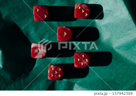 Red marble dice with gold heart pips on green crumpled paper. Romantic gambling concept, Valentine's Day luck, high contrast shadows art photography. Red marble dice with gold heart pips on green crumpled paper. Romantic gambling concept, Valentine's Day luck, high contrast shadows art photography. 137942389