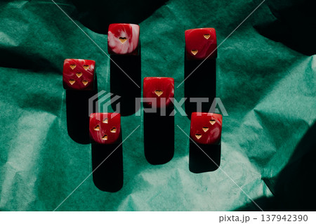 Red marble dice with gold heart pips on green crumpled paper. Romantic gambling concept, Valentine's Day luck, high contrast shadows art photography. Red marble dice with gold heart pips on green crumpled paper. Romantic gambling concept, Valentine's Day luck, high contrast shadows art photography. 137942390
